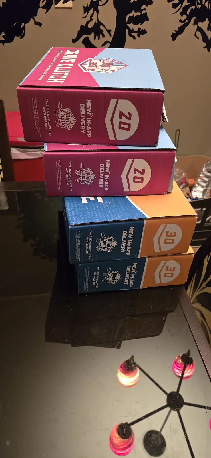 Four White Castle burger boxes are stacked on a glass table, two labeled '20' and two labeled '30', with the top box reading…