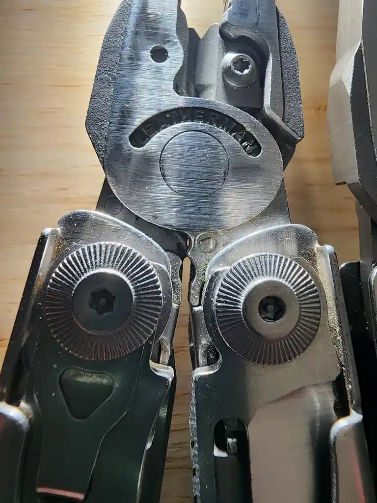 A close-up photo shows the open jaws of a well-used Leatherman multi-tool, revealing its internal gears and screws. The…