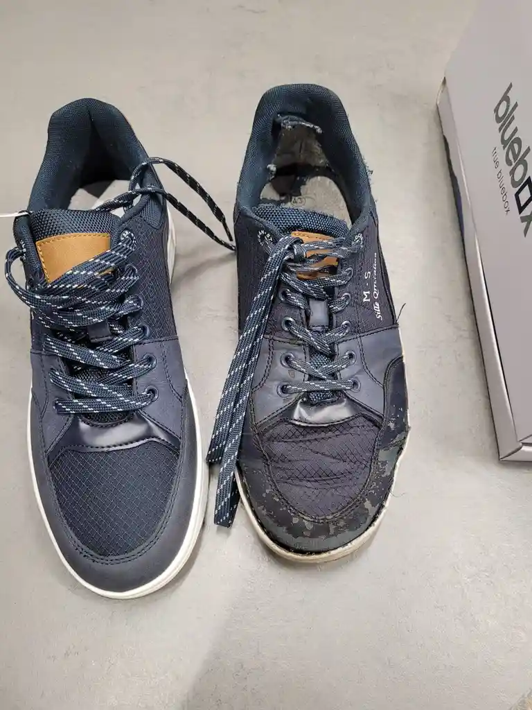 A top-down photo shows a pair of navy blue sneakers side-by-side on a gray surface; the left shoe is brand new and clean…