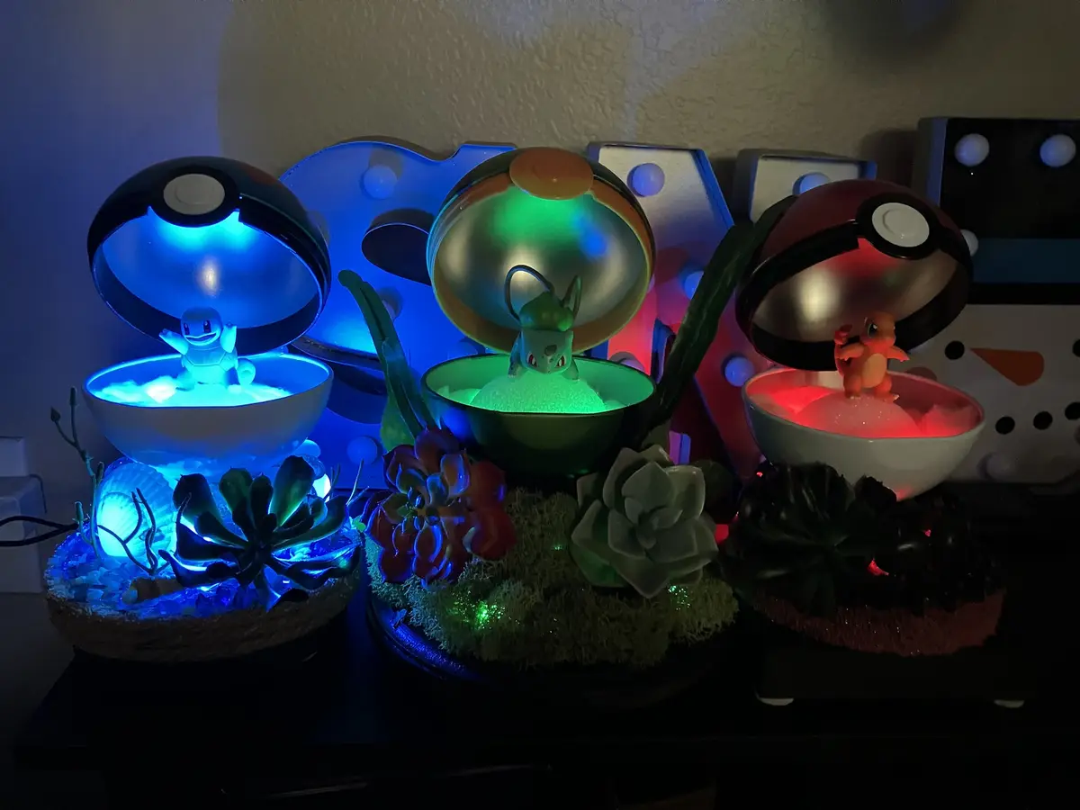 Three illuminated Pokémon-themed decorative displays feature Squirtle, Bulbasaur, and Charmander figurines emerging from…