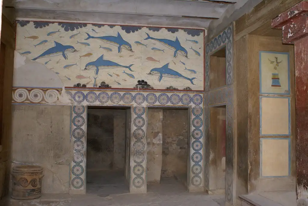 An ancient frescoed room, likely from Pompeii, features a large mural of blue dolphins leaping among fish on the upper wall…