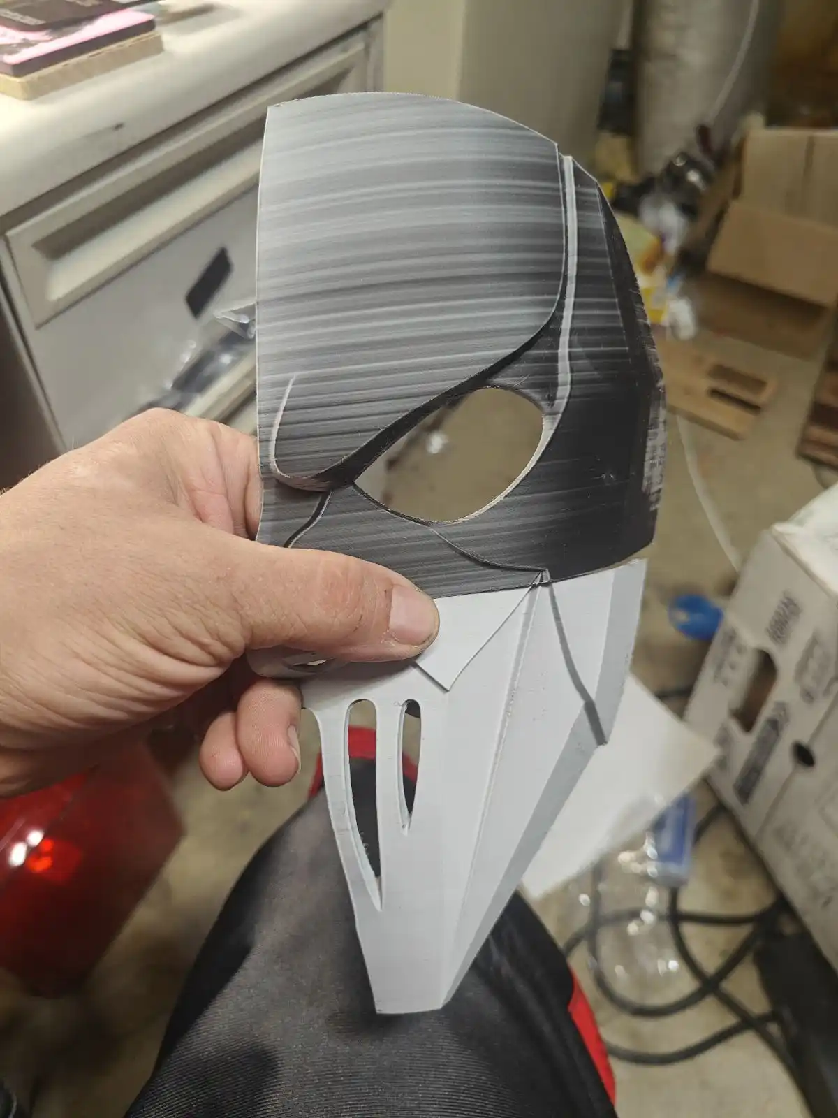 A hand holds up a 3D-printed mask resembling the iconic Ghostface from the 'Scream' movies, featuring a white lower half…