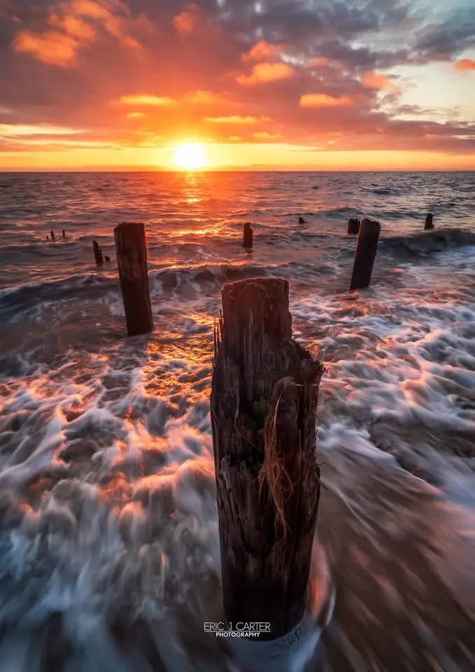 A serene sunset photograph shows the sun setting over the ocean, casting orange and pink hues across the sky and water…