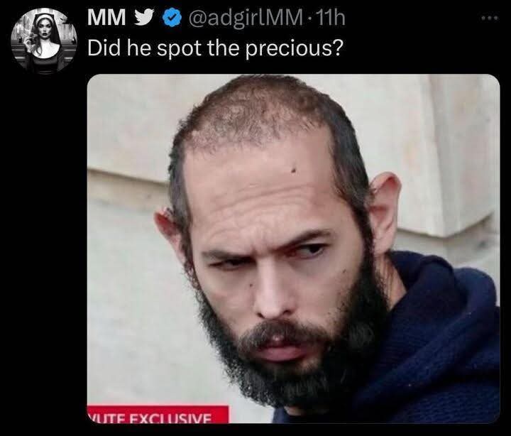 A close-up photo of a man with a receding hairline, a full beard, and a skeptical, narrowed-eyed expression. He wears a dark…