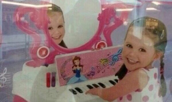 A young girl with pigtails smiles while playing a pink toy keyboard decorated with a Disney princess. Behind her, a pink toy…