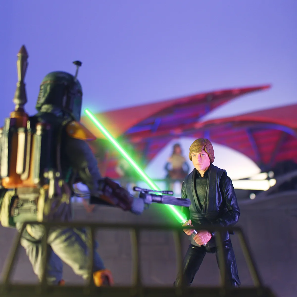 A photo of Star Wars action figures: Boba Fett in the foreground holding a green lightsaber, and Luke Skywalker in the…
