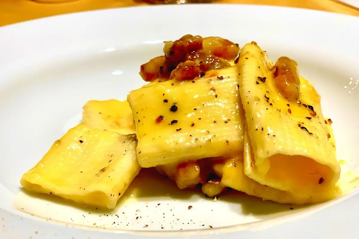 a close-up photo of a white plate holding several pieces of rectangular pasta, likely pappardelle or tagliatelle, covered in…