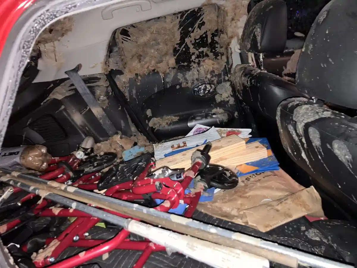 The trunk of a car is completely covered in brown mud and debris, with a red scooter, wooden planks, paper bags, and other…