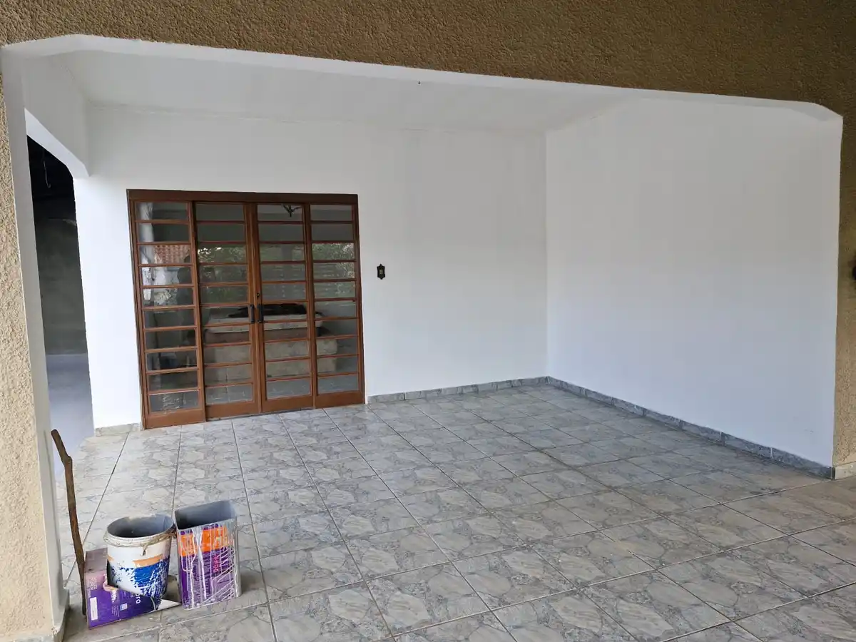 An empty, freshly painted room with white walls, tiled floor, and a wooden-framed glass door. Painting supplies including a…
