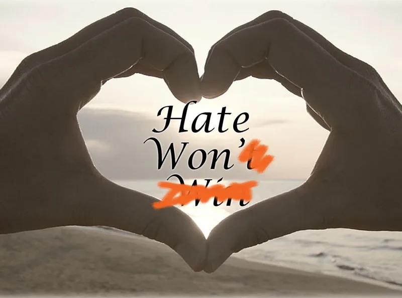Two hands form a heart shape against a beach sunset backdrop, with the text 'Hate Won't Win' overlaid. The word 'Win' is…