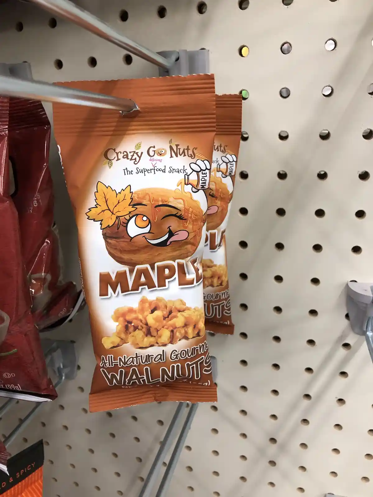 A close-up photo of a bag of 'Crazy Go Nuts' brand maple-flavored walnuts hanging on a store shelf. The packaging features a…