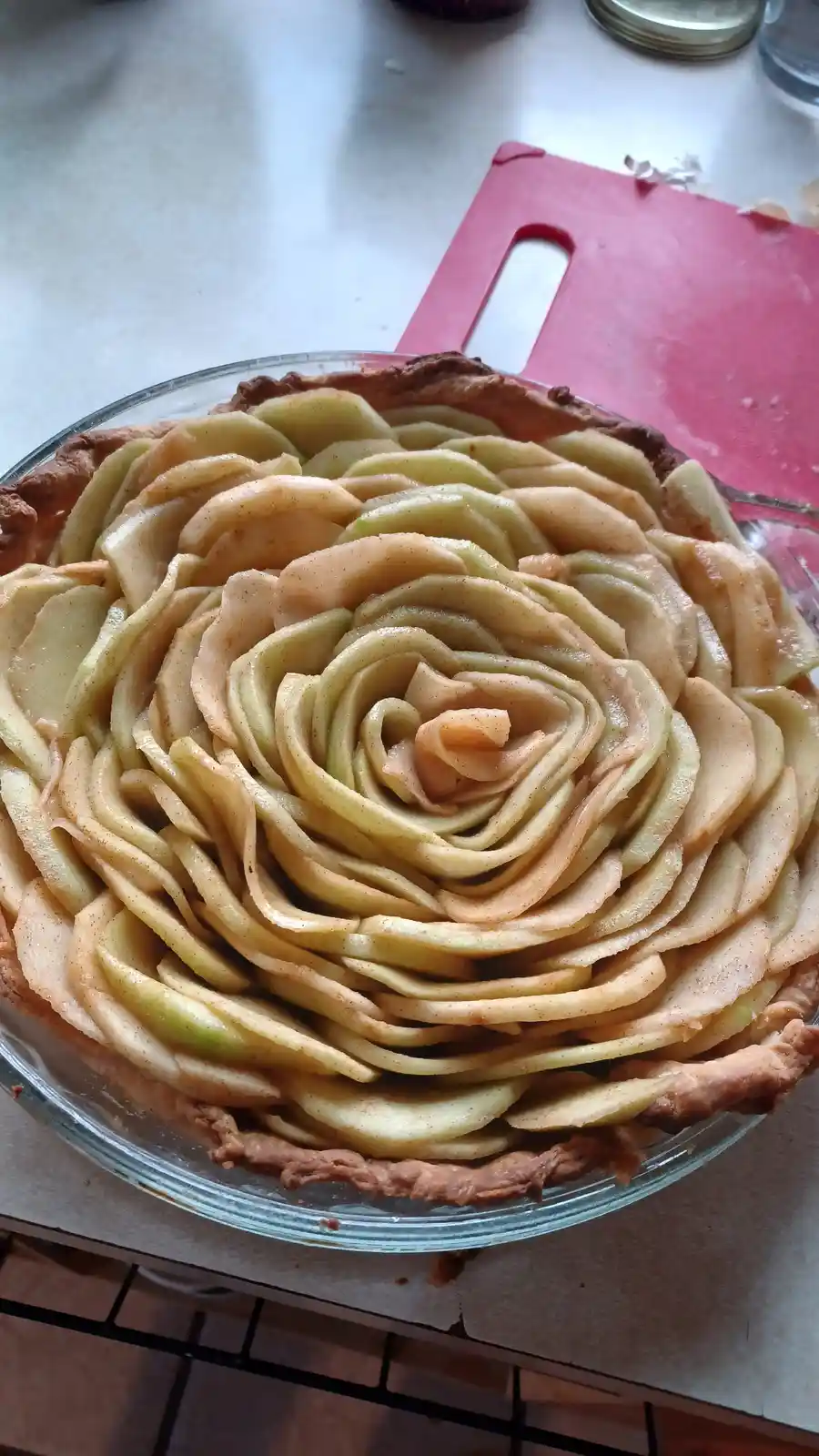 An apple pie with thinly sliced apples arranged in a rose-like pattern on top, sitting in a glass pie dish on a kitchen…