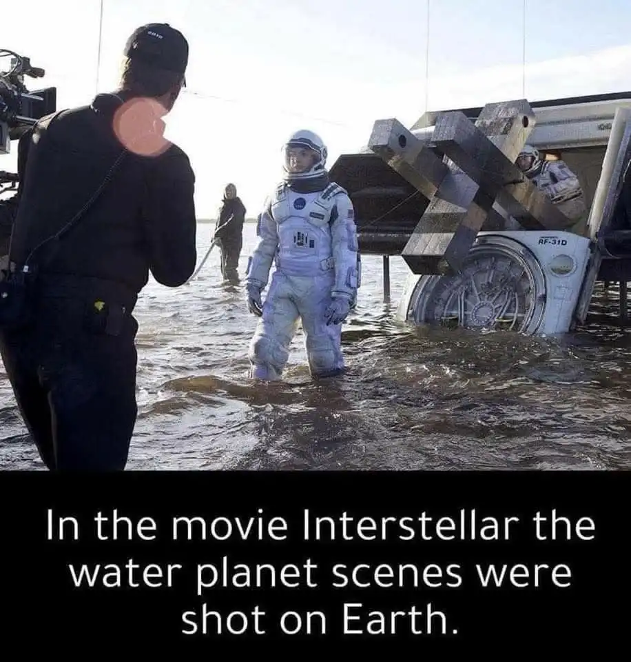 A behind-the-scenes photo from the movie Interstellar shows an actor in a full astronaut suit standing in shallow, muddy…