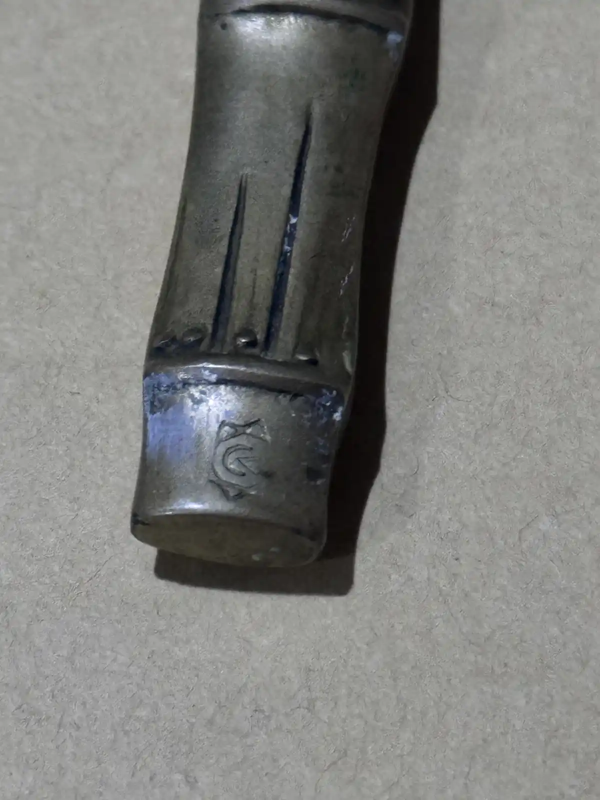 A close-up photo shows the metal handle of a hammer resting on a textured gray surface, with visible wear and a stamped logo…
