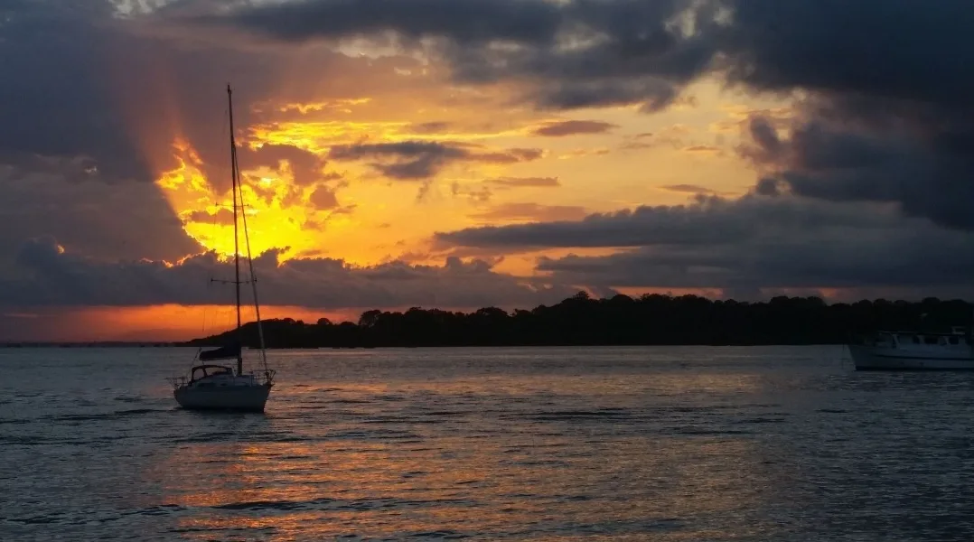 A serene sunset over water with a sailboat and another boat visible, featuring dramatic orange and dark clouds. The overlaid…