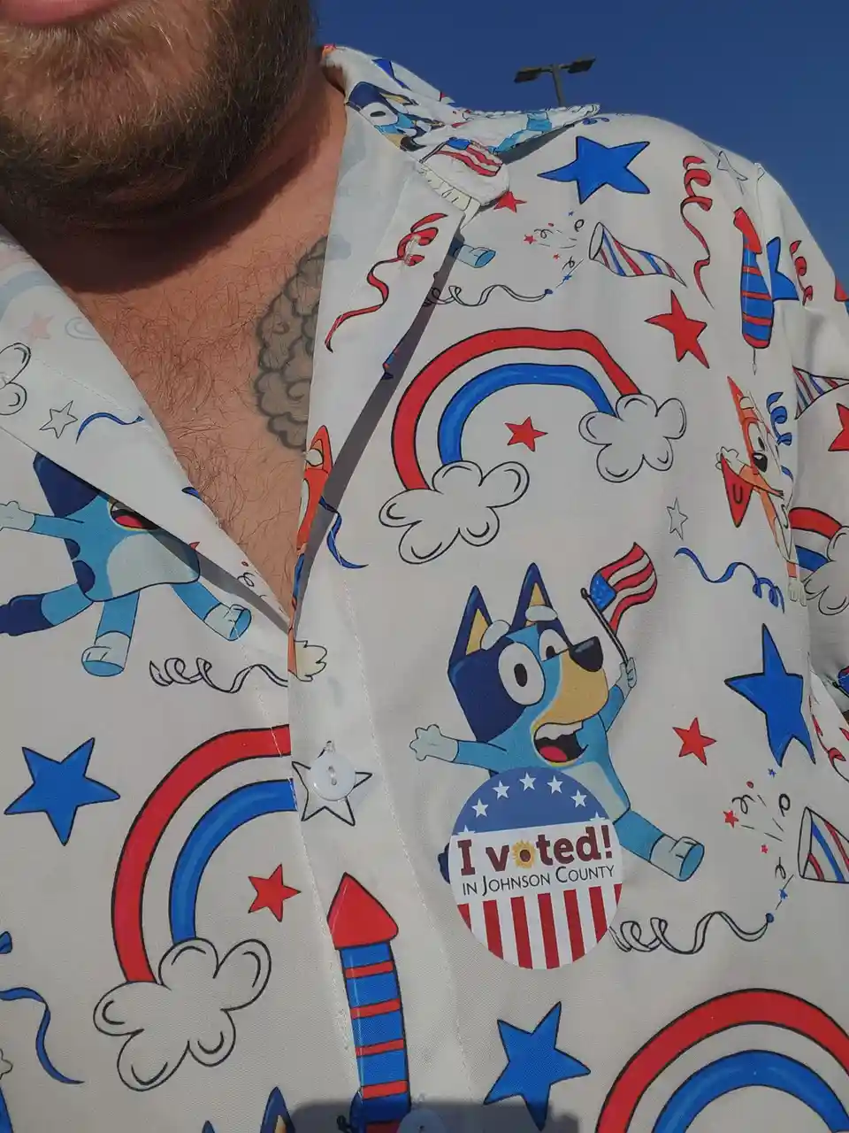 A close-up of a man's chest wearing a white button-up shirt covered in patriotic cartoon patterns including stars…