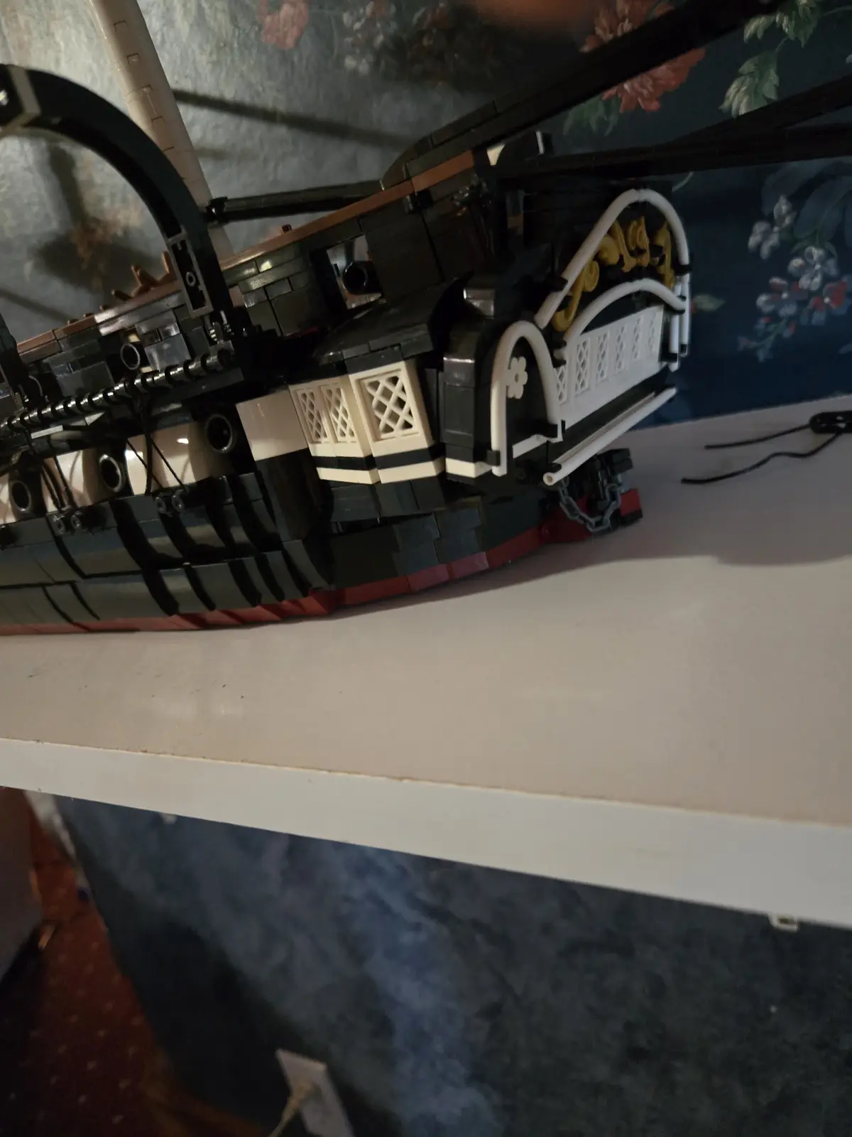 A close-up photo of a highly detailed LEGO model of a ship, featuring black, white, and gold pieces with intricate railings…