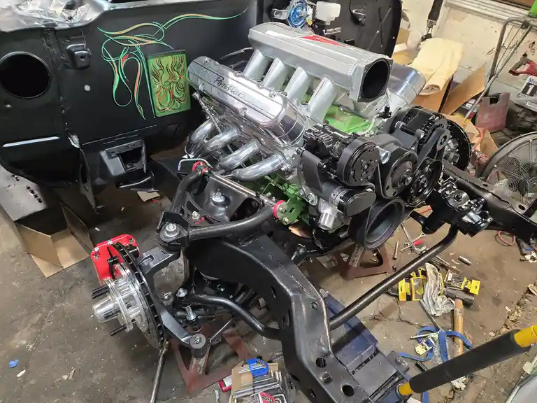 A high-performance Pontiac engine with chrome valve covers and green accents is mounted on a black car chassis in a…