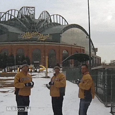 a six-panel image sequence shows three men in yellow Milwaukee Brewers jackets throwing snowballs at each other in front of…