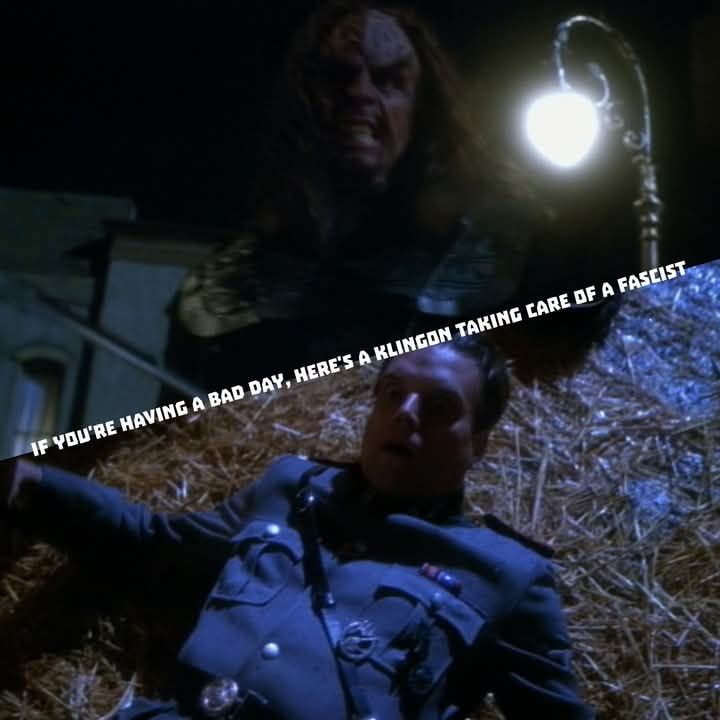 A man in a dark uniform lies on hay, looking up in shock, while a large, menacing Klingon warrior looms over him under a…