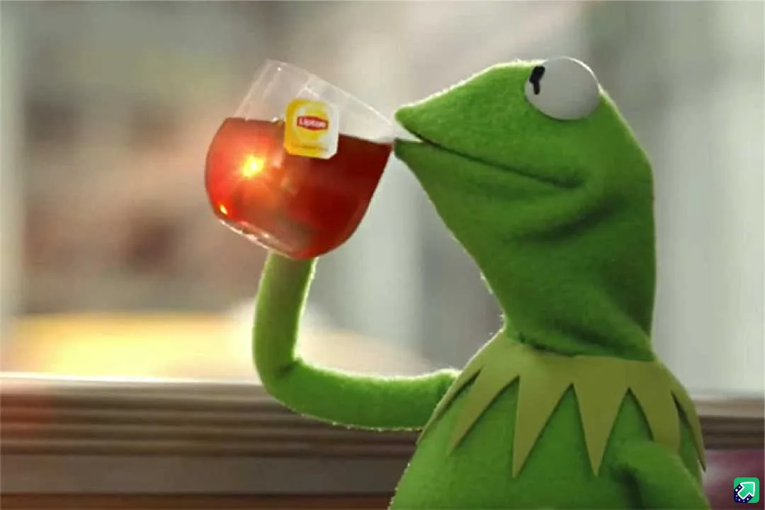 kermit the frog is shown sipping tea from a clear glass, with a lipton tea bag visibly steeping inside. the image captures a…
