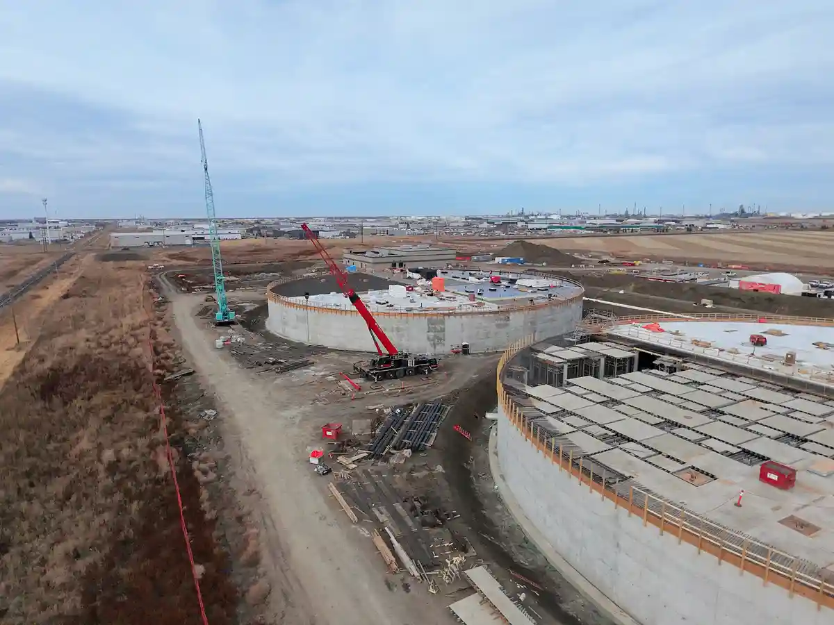 An aerial view of a large industrial construction site featuring two massive circular concrete structures under development…