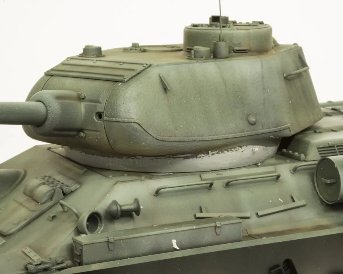 A close-up photo of a detailed green military tank model, showing its turret, gun barrel, and hull with visible weathering…