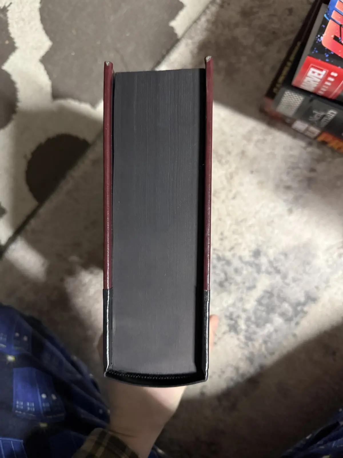 A person holds a thick, dark gray book with burgundy leather edges vertically, showing its spine and pages. The background…