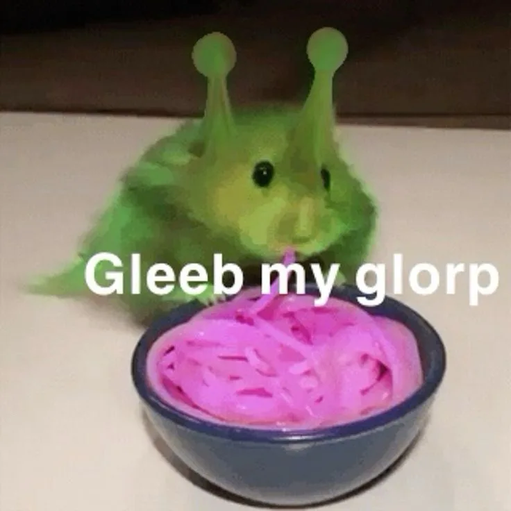 A green, fuzzy alien-like plush toy with two antennae is shown leaning over a blue bowl filled with pink, stringy, gooey…