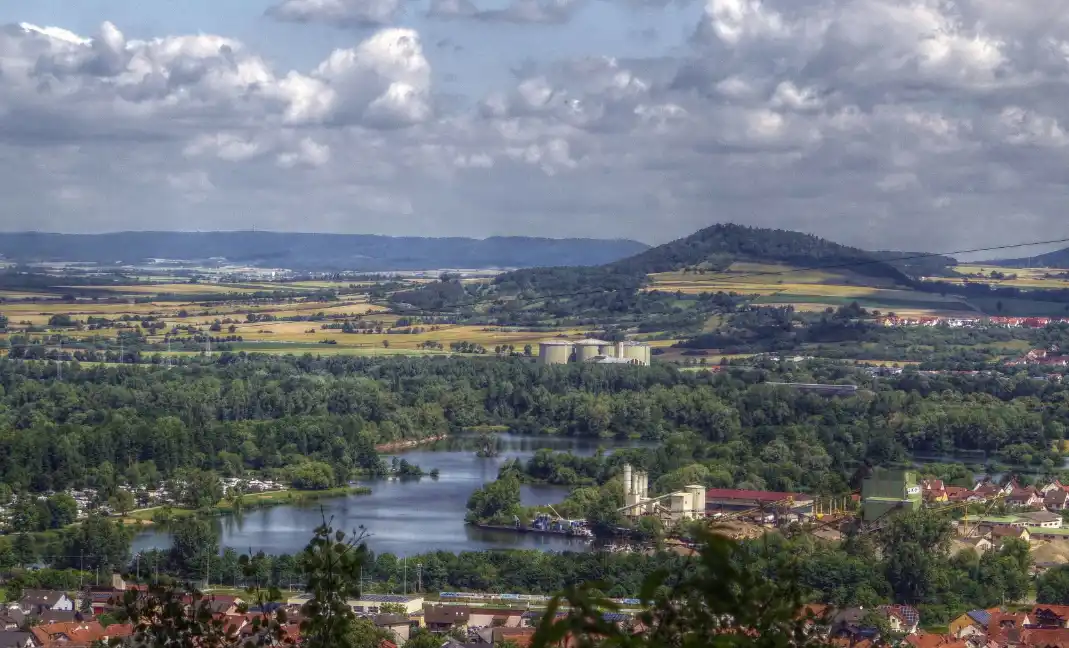 A scenic landscape photo showing a river winding through green forests and farmland, with towns and industrial silos visible…