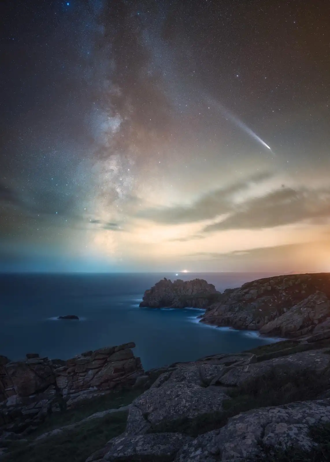A stunning night sky photograph shows the Milky Way galaxy arching across a star-filled sky above a rocky coastal landscape…