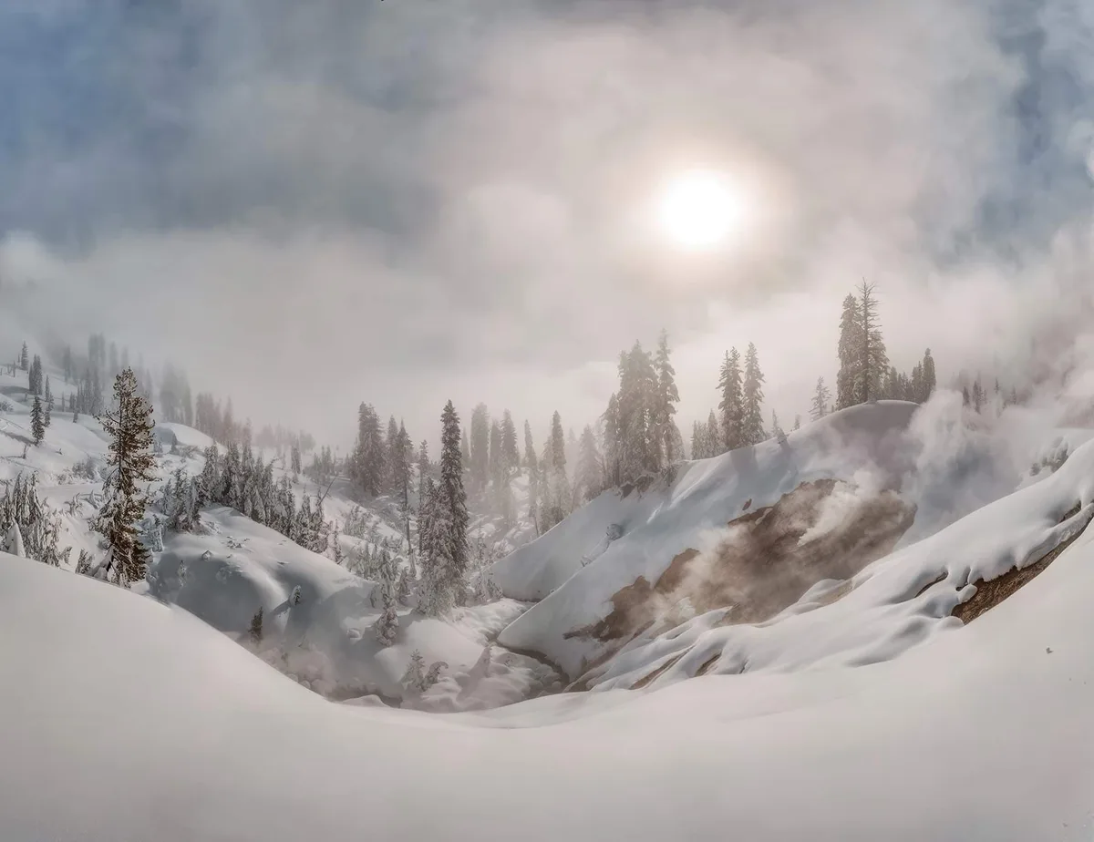 A snowy mountain landscape with evergreen trees, mist, and a bright sun partially obscured by clouds. Overlaid text reads…