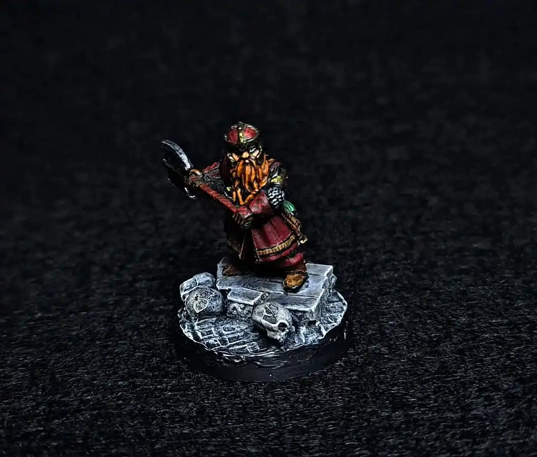 A painted miniature of a dwarf warrior with a long beard, wielding a large axe, standing on a rocky base adorned with…