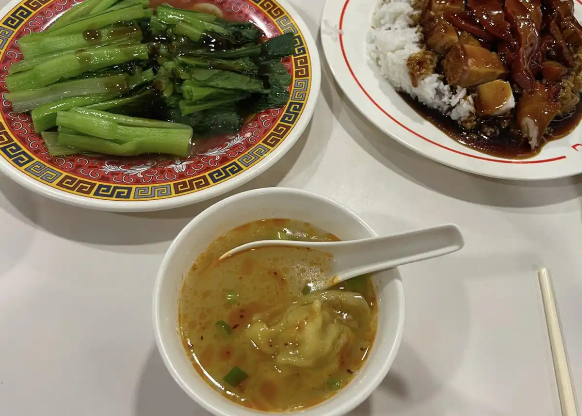A table setting shows three dishes: a plate of stir-fried green vegetables, a plate of rice with braised meat, and a bowl of…