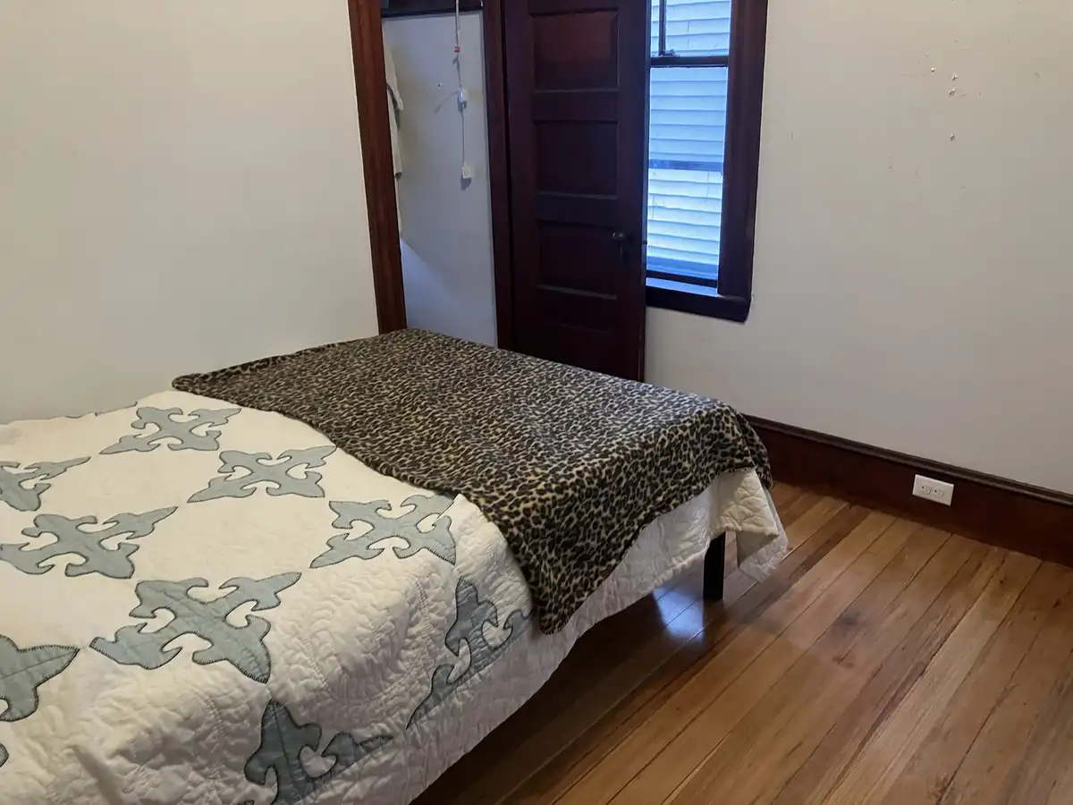 A simple bedroom scene featuring a bed with a white quilt adorned with gray geometric patterns and a leopard-print blanket…