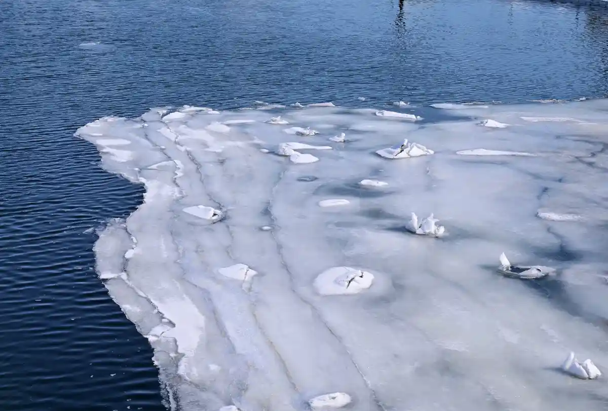 A photo shows a partially frozen body of water with broken ice floes and chunks floating on dark blue water. Overlaid text…