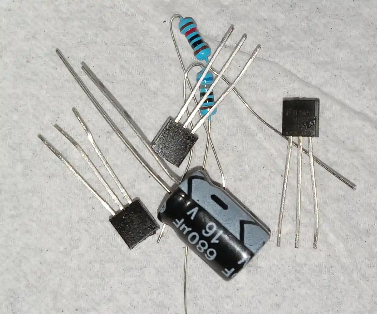 A close-up photo shows several electronic components—two black transistors, a blue resistor, and a black cylindrical…