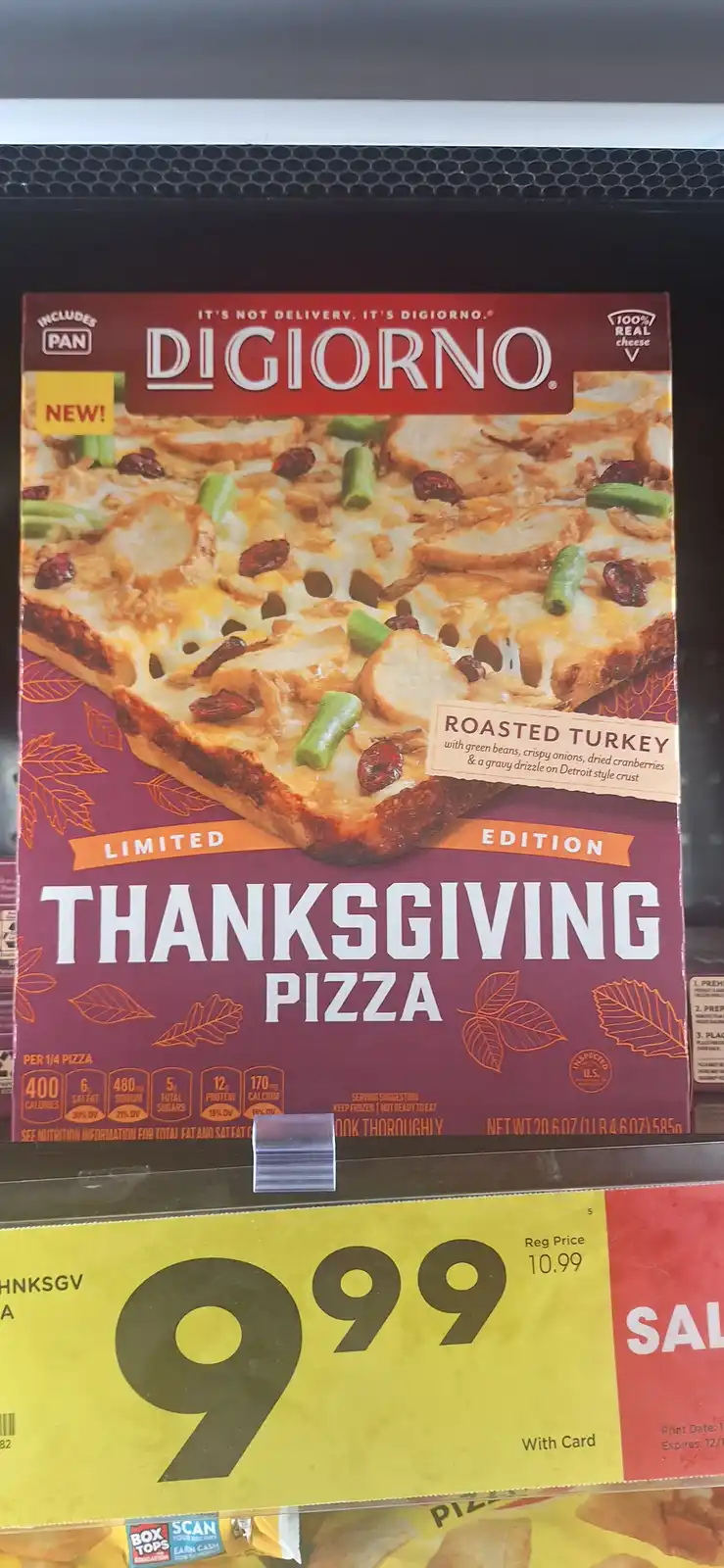 A close-up photo of a Digiorno Thanksgiving pizza box on a grocery store shelf, with a yellow price tag below showing '999'…