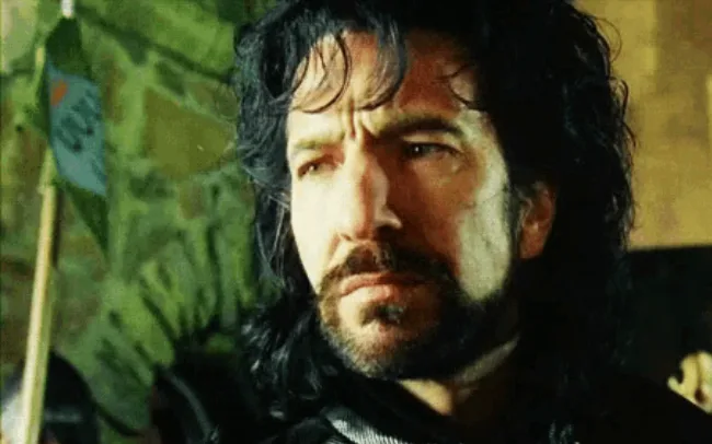 A man with long dark hair and a beard looks off to the side with a skeptical, unimpressed expression. He appears to be in a…