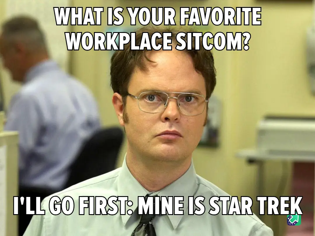 A man with glasses and a light-colored shirt stares intently at the camera in an office setting, with another person blurred…