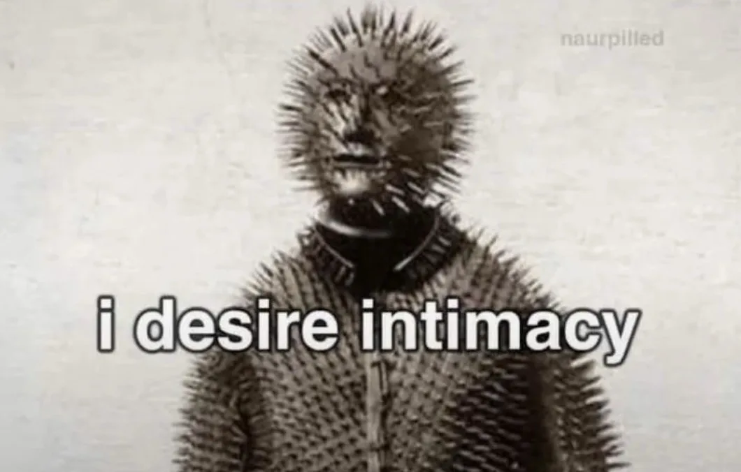 A black and white image shows a person covered in spines, resembling a porcupine or hedgehog, with a neutral expression. The…