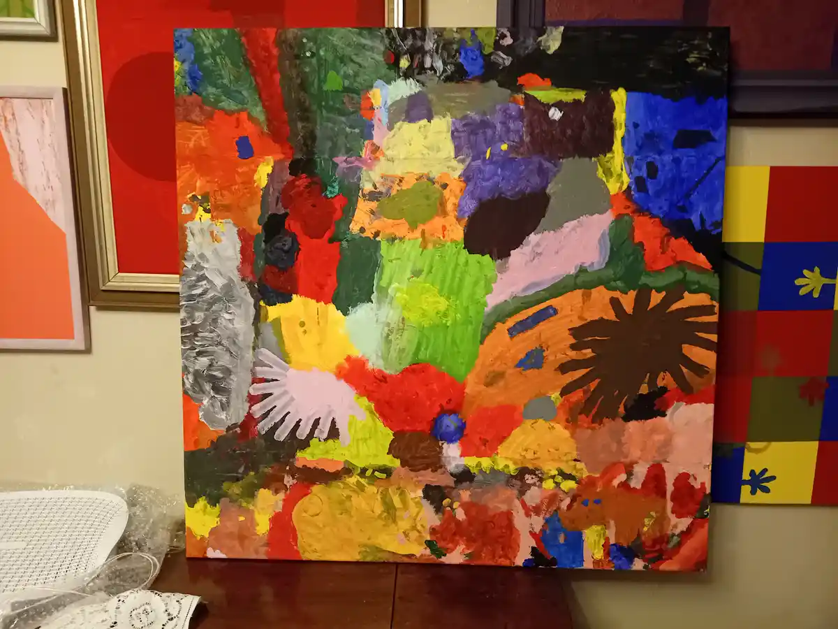 A colorful, abstract painting with thick, textured brushstrokes in red, green, blue, yellow, and black sits on a wooden…