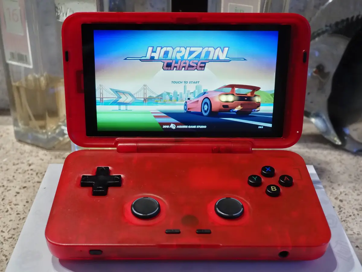 A red handheld gaming device displays the title screen of the game 'Horizon Chase,' featuring a pink sports car on a track…