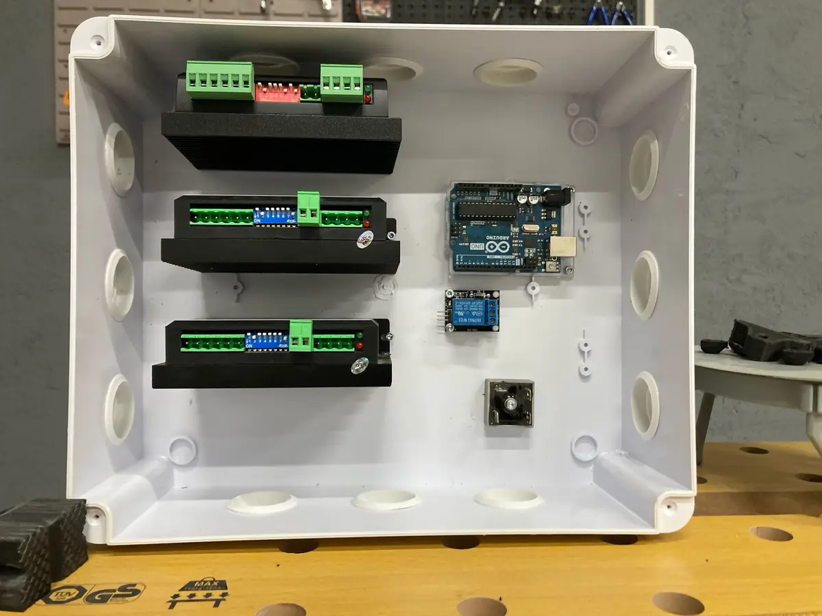 A white plastic electronics enclosure contains an Arduino Uno board, a relay module, and three black terminal blocks with…