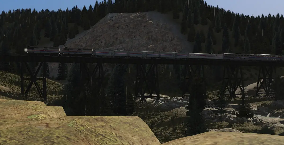 A train with Amtrak branding travels across a wooden trestle bridge through a forested mountain valley. The overlaid text…