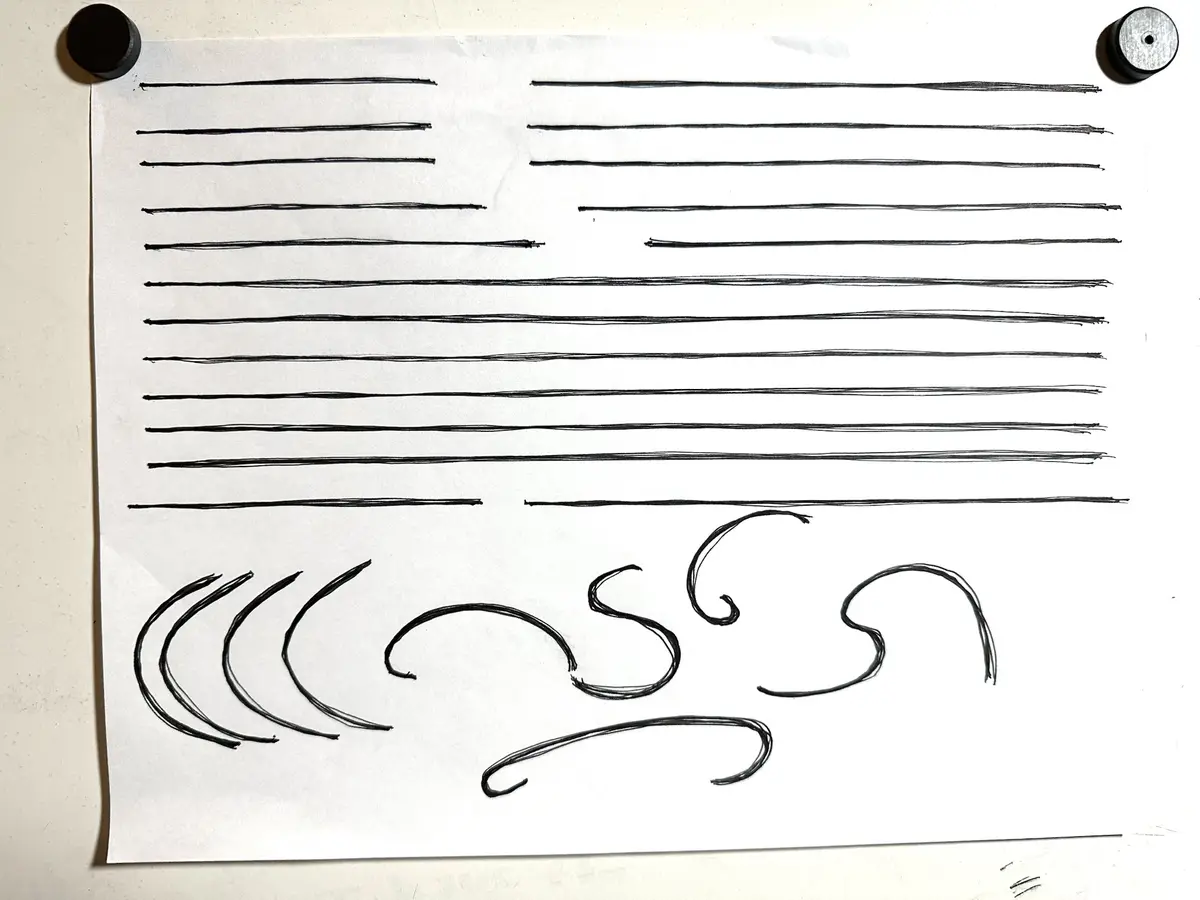 A white sheet of paper pinned to a surface with two magnets, featuring multiple horizontal black lines resembling text, with…