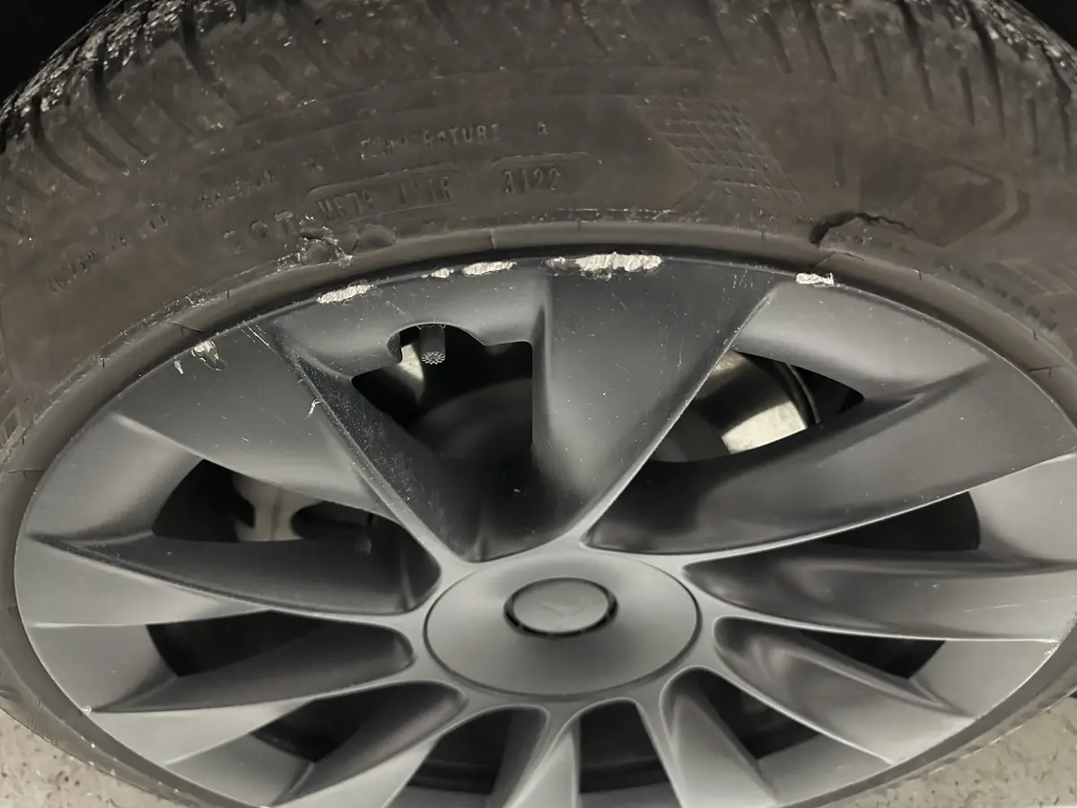 A close-up photo of a car's wheel and tire, showing visible damage: the tire has a large crack near the rim, and the rim…