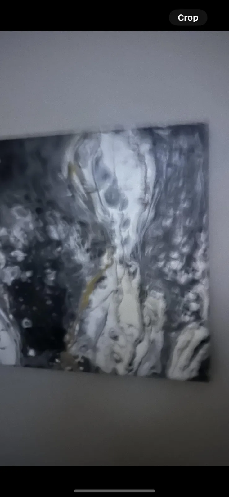 A close-up photo of a modern abstract painting with swirling gray, white, and black patterns, hanging on a plain wall. The…