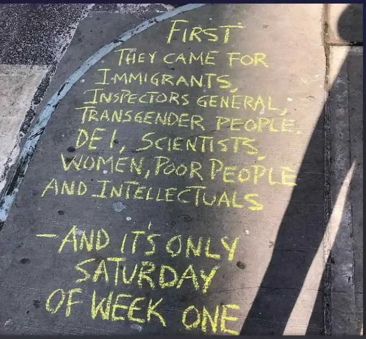 Yellow chalk writing on a dark pavement surface lists a series of groups including immigrants, inspectors general…