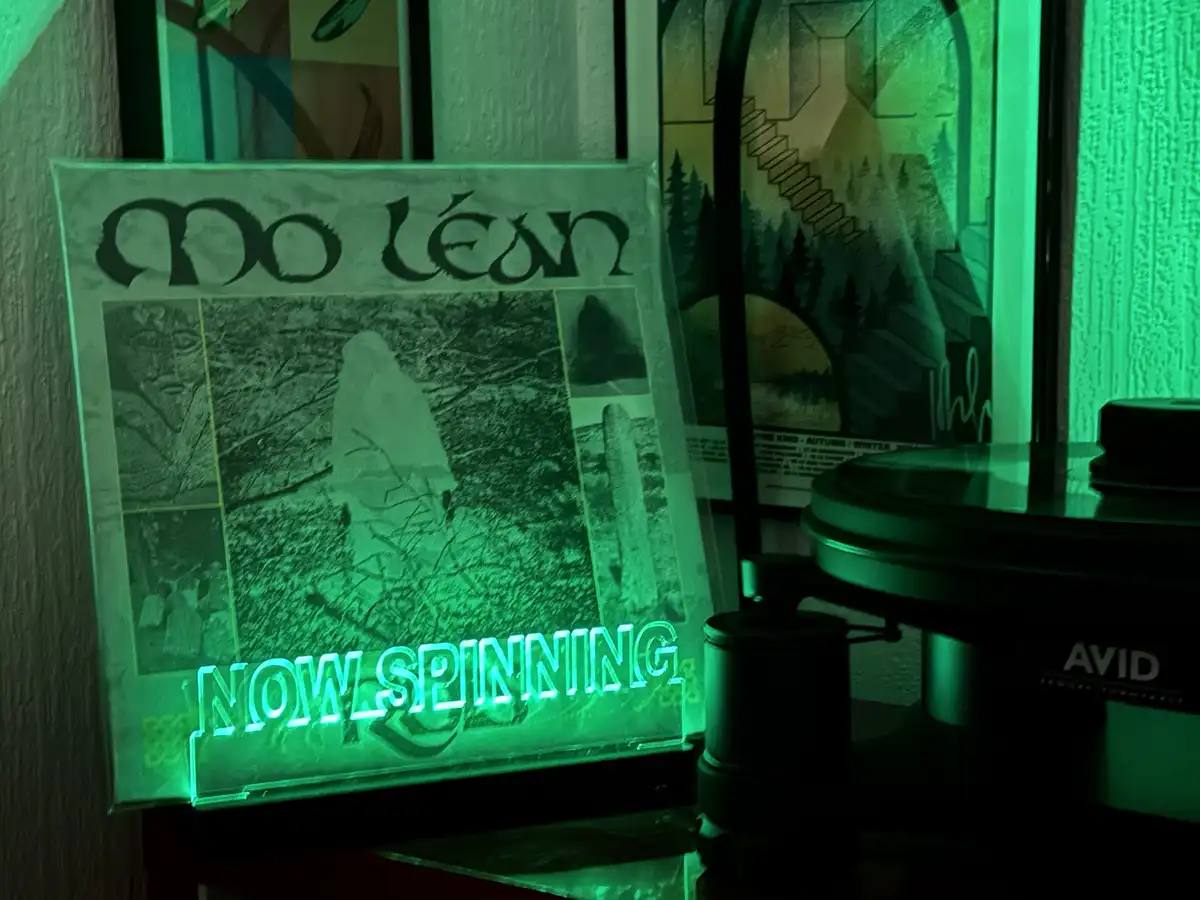 A green-lit vinyl record sleeve for the band 'Mo Léan' is displayed next to a turntable, with the glowing text 'NOW…